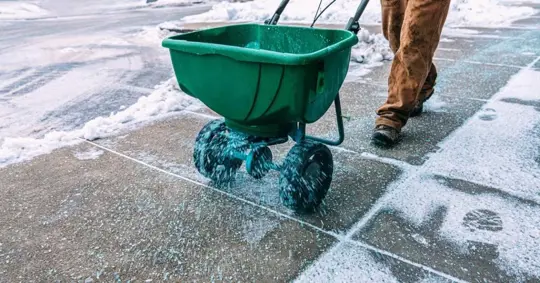 Maintenance Worker spreading Ice-Melting Calcium Chloride Salt on a Sidewalk