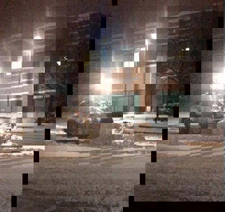 A snowplow clears a parking lot on a snowy night.