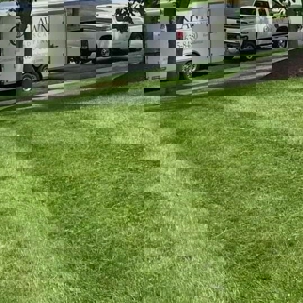 A landscaping company truck and trailer are parked on a green lawn