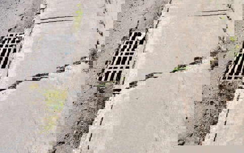 An outdoor shot shows a cracked sidewalk next to a storm drain