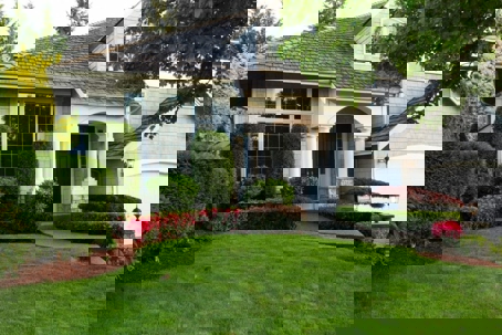 A well-maintained home with lush landscaping, including manicured bushes, a vibrant red flower bed, and a neat lawn