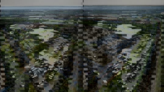 Overhead view of commercial property with trucks parked in rows, surrounded by trees.