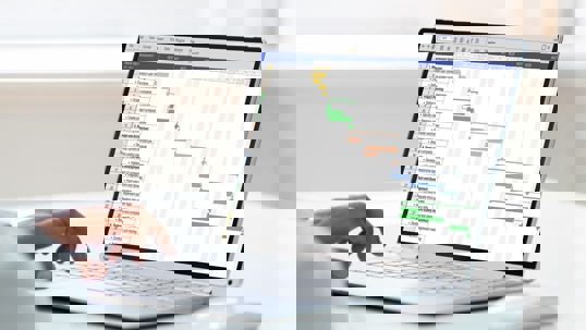A person types on a laptop displaying a Gantt chart