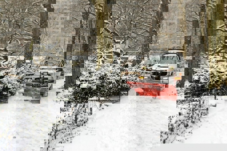 a white pick-up truck with a red snowplow clears a snow-covered path in Central Park