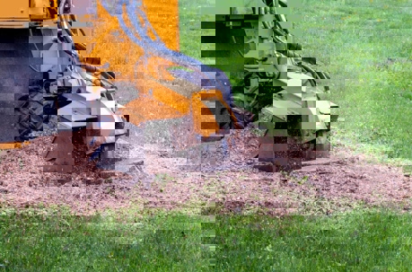 A yellow stump grinder is shown in use, removing a tree stump in a grassy yard.