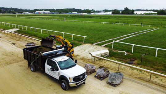 A landscape project is underway; a truck and digger are working on the site of a racetrack.