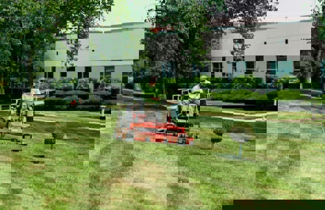 A person mows a large green lawn on a riding lawn mower.