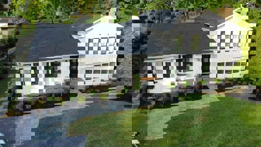 a white house with black window trim, a dark grey roof, and a well-manicured lawn and landscaping.