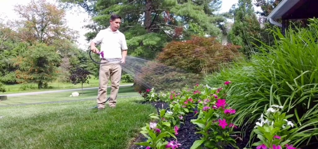 A man waters a flower bed in a green lawn
