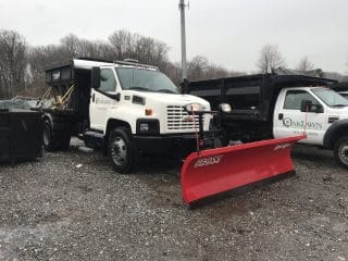A white truck, used for snow removal is parked outside on gravel
