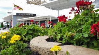 A ground-level shot showcases red and yellow flowers blooming in front of a "CLUBHOUSE" building, where a Maryland flag is visible.