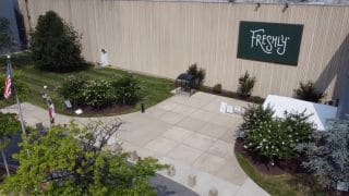 A lush lawn and well-tended garden highlight the "Freshly" brand logo on a building's exterior wall.