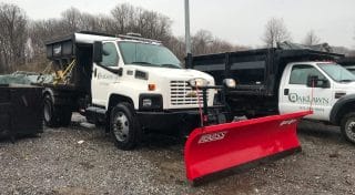 A white Oak Lawn Landscaping snowplow truck is parked