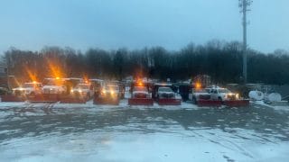 A row of snowplows are lined up on a snowy lot