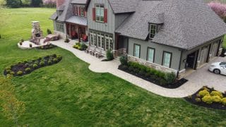 Landscape design of a home features a stone patio with an outdoor fireplace and seating area.