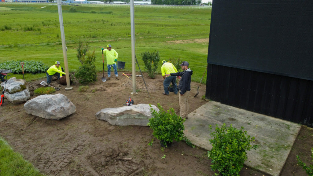 Landscapers in bright yellow shirts are working on landscaping around a building