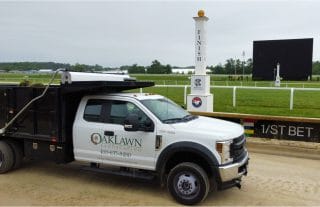A white Oaklawn Landscaping truck parked by a racetrack finish line.