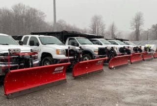 A line of municipal snowplow trucks, equipped with red plows are aligned i