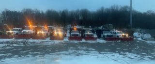 A line of snow plows with orange blades is parked in the snow.