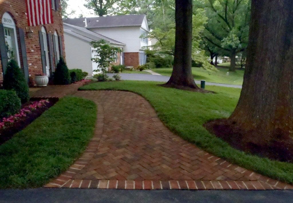 A brick pathway stretches between trees and lawn