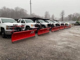 A row of Oaklawn Landscaping's white trucks with red snowplows are parked