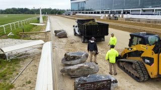 Landscapers place decorative rocks along a track at a racecourse